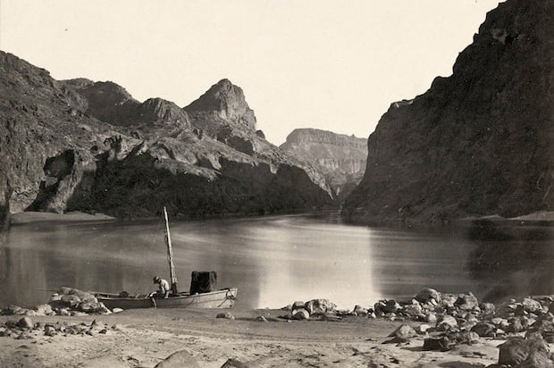 Man in a wooden boat on the edge of the Colorado River in the Black Canyon, Mojave County, Arizona. Taken in 1871.