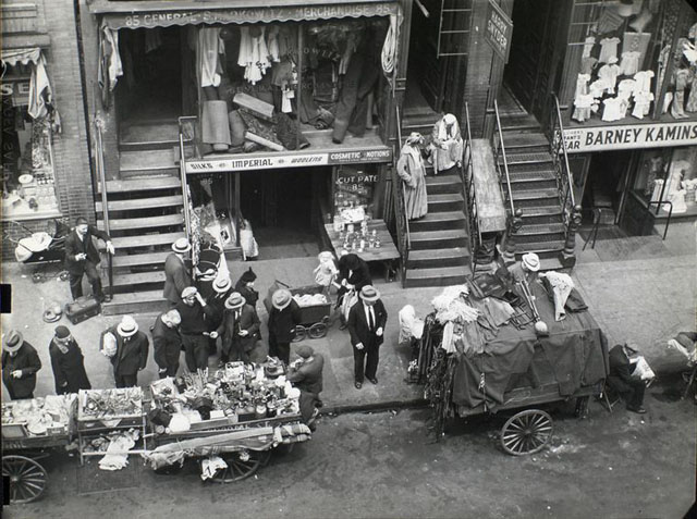 Hester Street, between Allen and Orchard Streets, Manhattan. Looking down from window on street scene including peddlers, women sitting on stoop, baby carriages, fabric and clothing stores and pedestrians.