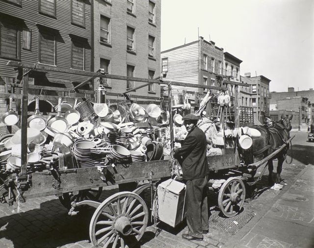 Travelling tin shop, Brooklyn. Tinker looks over his shoulder at camera while he ties box to wagon already loaded with pans, brushes, basins, etc.