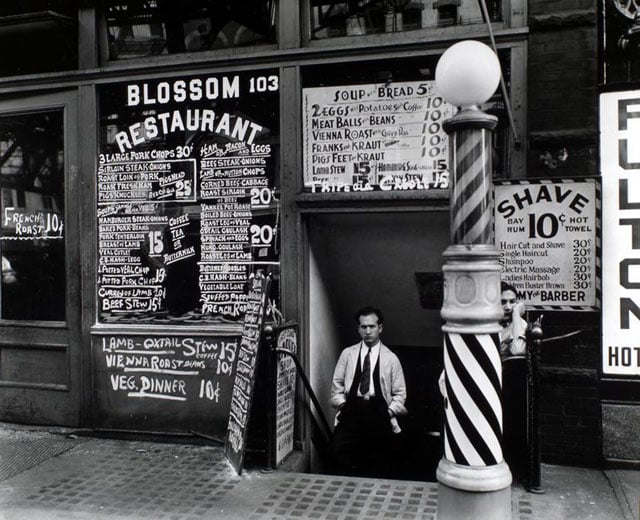 Blossom Restaurant, 103 Bowery, Manhattan. Men stand at entrance to barbershop, pole in front, under the Blossom Restaurant, which has menu painted on windows and board out front.