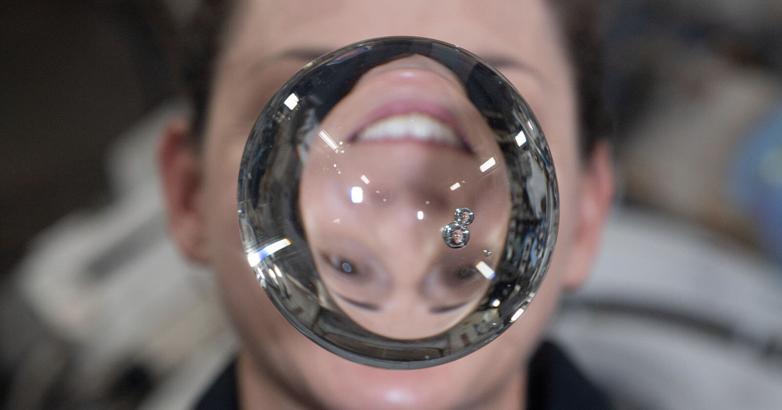Astronauts Image Refracted Through a Weightless Water Bubble in Space