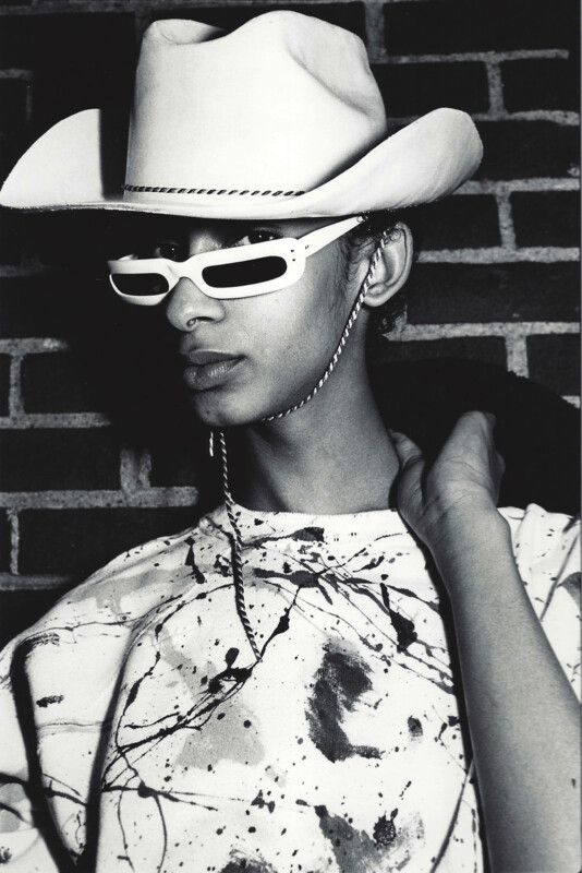 A man in a cowboy hat looks at the camera from above his sunglasses.