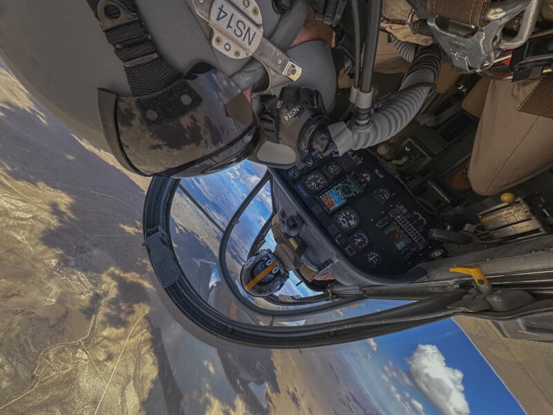 View from inside a helicopter cockpit showing the pilot’s viewpoint, with controls visible and a barren landscape visible through the glass below.