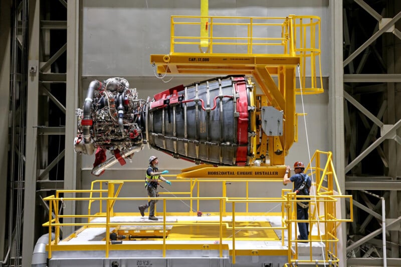 Engineers working on a large rocket engine, which is being installed horizontally in a high-tech industrial setting, surrounded by structural metal frameworks and safety platforms.