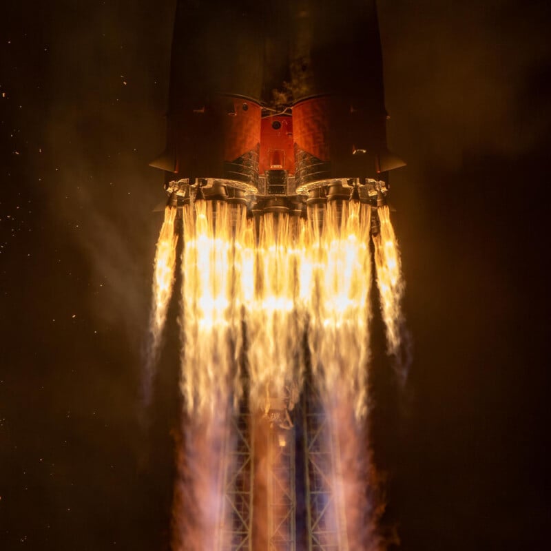 Close-up view of a rocket launch showing intense flames and smoke emitted from the engines against a dark background.