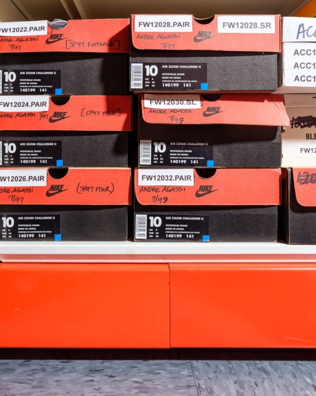 Stacked Nike shoe boxes labeled "Air Zoom Challenge II" with various codes and "Andre Agassi" written on them, sitting on a bright orange shelf.