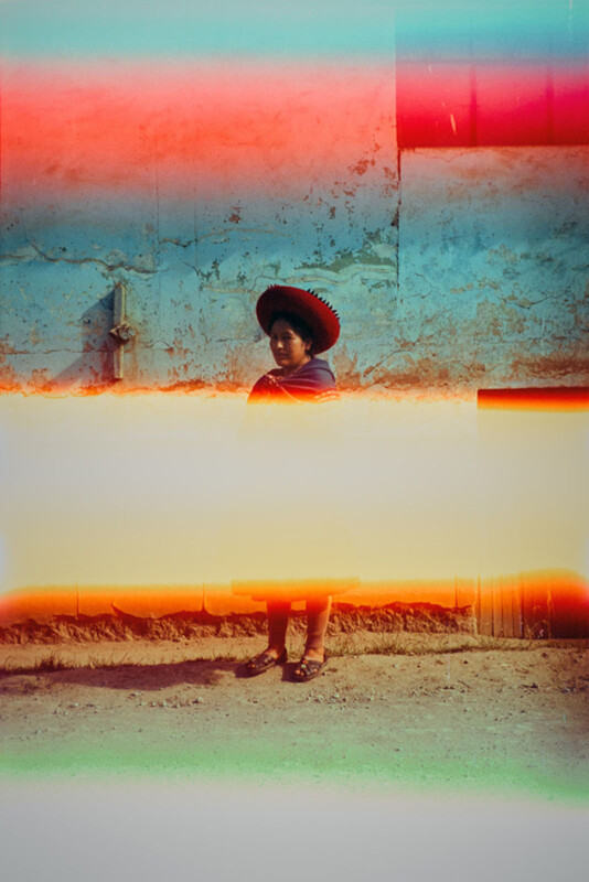 A person in traditional clothing and a wide-brimmed hat stands against a worn blue wall. Colorful light leaks and film burns partially obscure the image, creating vivid bands of red, yellow, and blue.