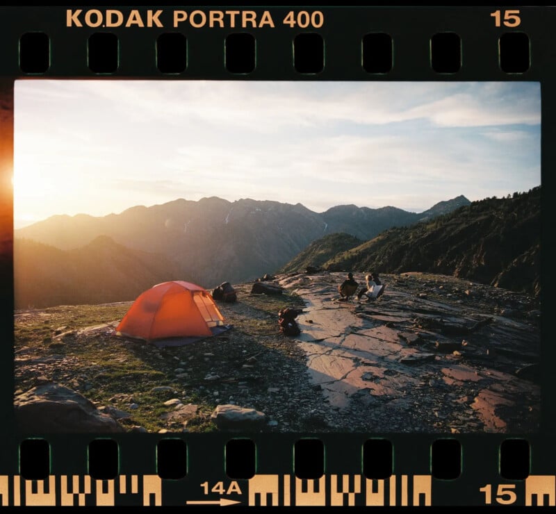 An orange tent sits on a grassy mountain plateau at sunset, with people sitting nearby. Rugged mountains and a partly cloudy sky are in the background. The image has a vintage film border labeled "KODAK PORTRA 400.