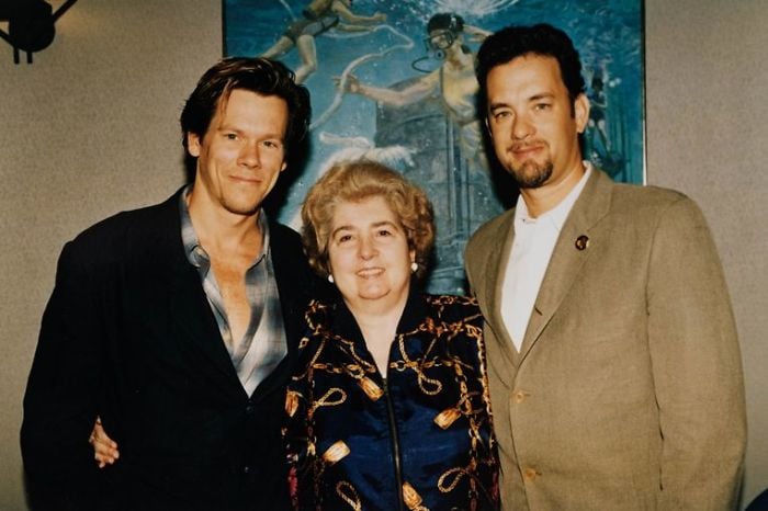 Three people stand together, smiling for the camera. Two men stand on either side of a woman. Behind them is a painting depicting underwater divers and marine life.