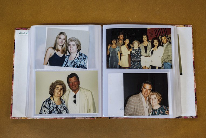 An open photo album displays several pictures of an older woman posing with various people, including a young woman and men, all smiling together against different backdrops, on a brown surface.