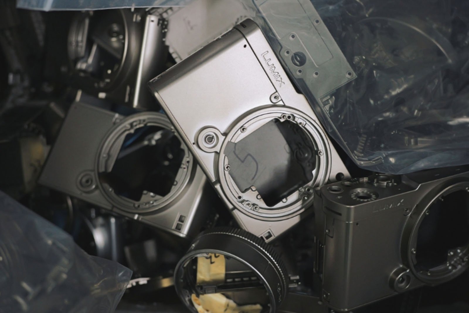 A pile of silver and gray metal camera bodies without lenses, surrounded by plastic packaging, showing the internal structure and components of the cameras.