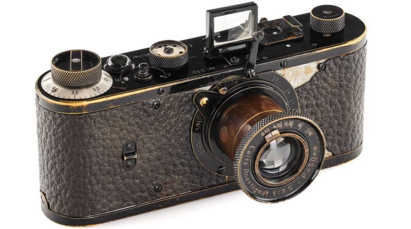 A vintage Leica camera with a brown leather-textured body, metal dials, and a protruding lens labeled "Leitz Elmar 1:3.5 f=50mm." The camera shows signs of wear and age.