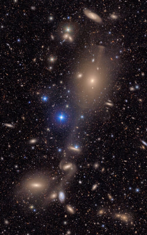 A deep-space image showing numerous galaxies, both spiral and elliptical, scattered across a star-filled background with a few bright, glowing galaxies dominating the center and lower part of the scene.
