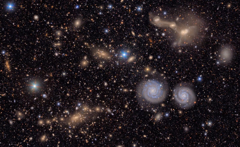 A dense star field with numerous galaxies of varying shapes and sizes, including two prominent spiral galaxies near the center right against a dark background. The image captures the vastness of deep space.