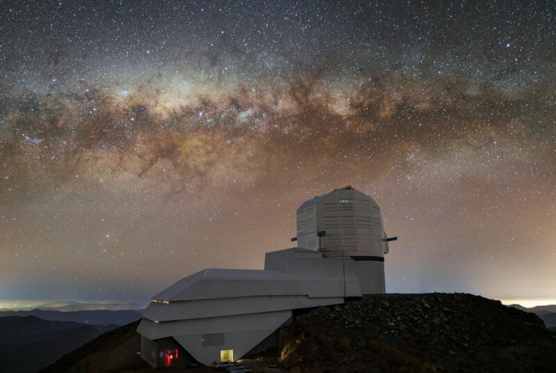 A large astronomical observatory sits on a rocky mountain under a clear night sky filled with stars and the bright band of the Milky Way galaxy.