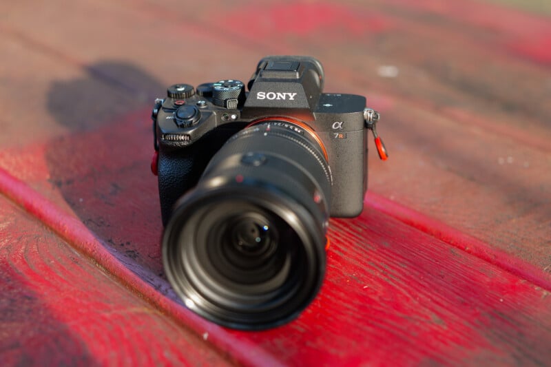 A Sony Alpha 7 III digital camera with a large lens sits on a weathered red wooden surface, captured in natural outdoor lighting.