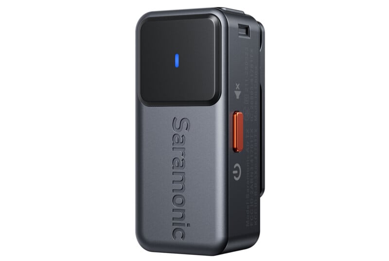 A compact, rectangular Saramonic wireless microphone transmitter in dark gray with a black top, a single blue LED indicator, and an orange button on the side.