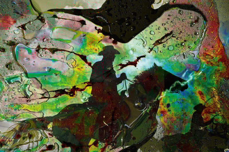 A silhouette of a person riding a horse is seen against a colorful, abstract background with splashes of green, red, and yellow, along with water droplets and swirling patterns.