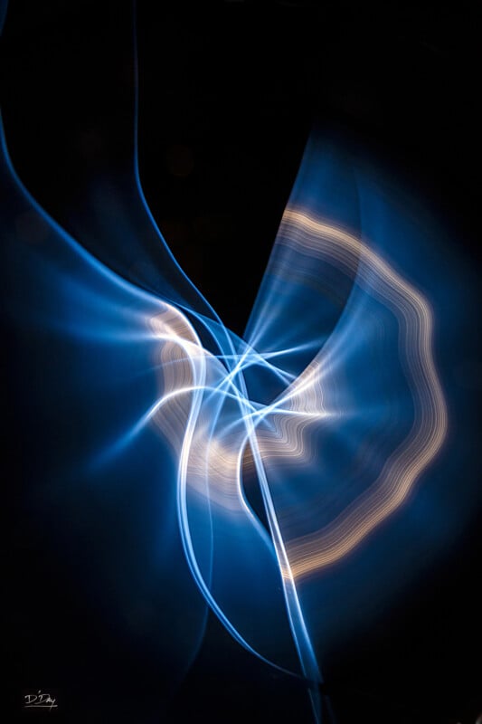 Abstract image featuring swirling blue and white light trails against a dark background, creating a dynamic, fluid, and ethereal visual effect.