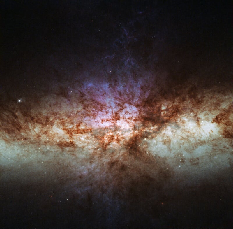 A cosmic scene showing a bright, colorful galaxy with dense dust lanes, glowing purple and orange clouds, and scattered stars against the dark backdrop of space.