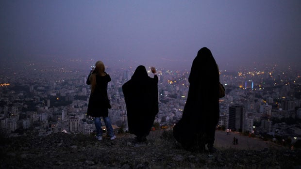 Women in the hills above Tehran at dusk. Concealing clothing in the Islamic Republic, including head coverings, is mandatory for women, but the exact definition of "modest" is flexible, leading to a tug of war between young females and the authorities each spring. Outside metro stations female police can be seen regularly checking the passers by.  If a woman's dress is considered "immodest" she is arrested and taken into custody. In 2010 a senior cleric in Tehran blamed the frequency of earthquakes in Iran on women who "lead young men astray" with their revealing clothing.