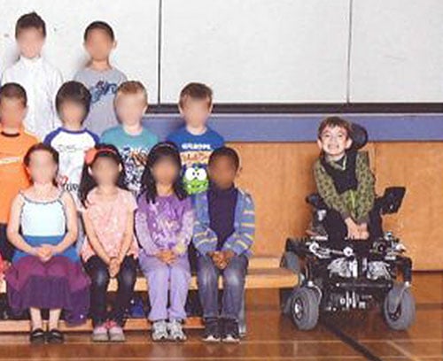 Miles Ambridge posing to the side of the bench his classmates are sitting on.