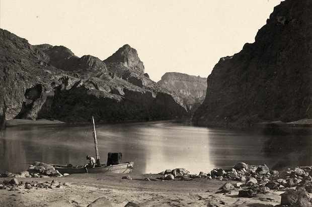 Man in a wooden boat on the edge of the Colorado River in the Black Canyon, Mojave County, Arizona. Taken in 1871.