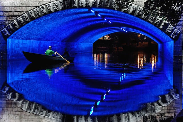 Eye on Riga: A bridge in the Latvian capital glows neon indigo as boaters row back to the docks at night. Photo ©Mike Randolph