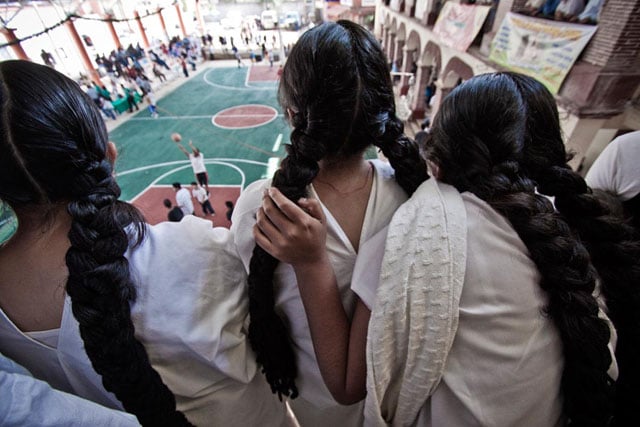 Indigenous Zapotec girls in traditional costume watch a basketball game in San Cristobal Lachiroag.