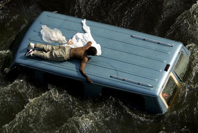 A man clings to the top of a vehicle before being rescued by the U.S. Coast Guard from the flooded streets of New Orleans, in the aftermath of Hurricane Katrina, in Louisiana, September 4, 2005. Robert Galbraith.