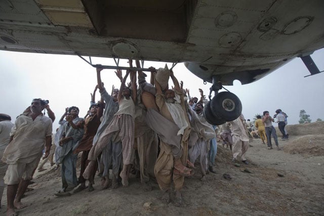 Marooned flood victims try to grab onto the side bars of a hovering army helicopter which arrived to distribute food supplies in the Muzaffargarh district of Pakistan's Punjab province, August 7, 2010. Adrees Latif.