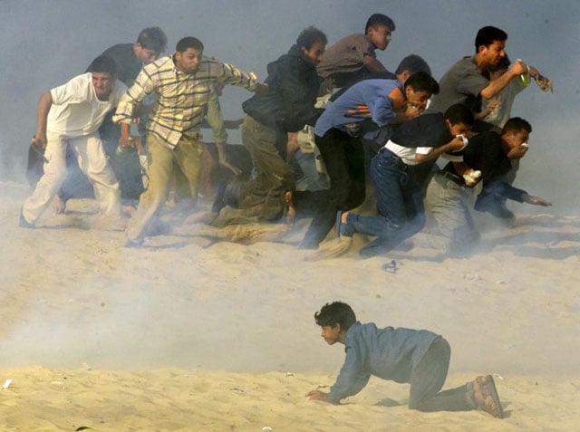 Palestinians try to run away from Israeli soldiers firing teargas during Palestinian-Israeli clashes in the southern Gaza Strip town of Khan Younis, October 20, 2000. Reinhard Krause.