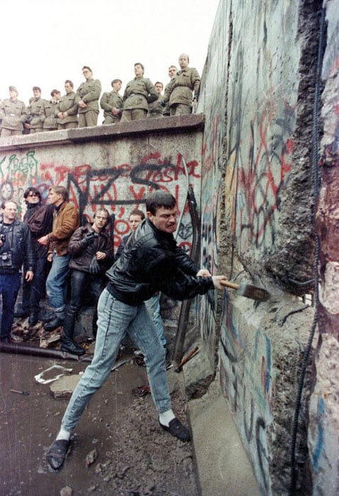 A demonstrator pounds away at the Berlin Wall as East Berlin border guards look on from above the Brandenburg Gate in Berlin, November 11, 1989. David Brauchli.