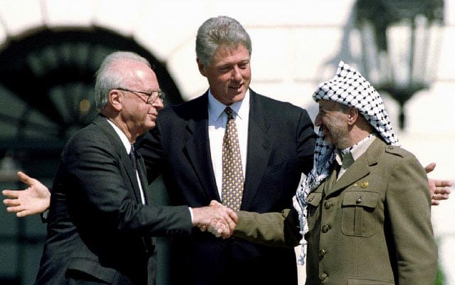 U.S. President Bill Clinton looks on as Israeli Prime Minister Yitzhak Rabin and Palestine Liberation Organization leader Yasser Arafat shake hands after the signing of the Israeli-PLO peace accord at the White House, September 13, 1993. Gary Hershorn.