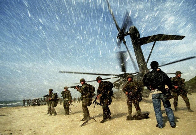 An Albanian man carries a child to a US Marine CH53 Super Stallion helicopter as it lands at Golame beach near the port of Durres, March 16, 1997. Yannis Behrakis.