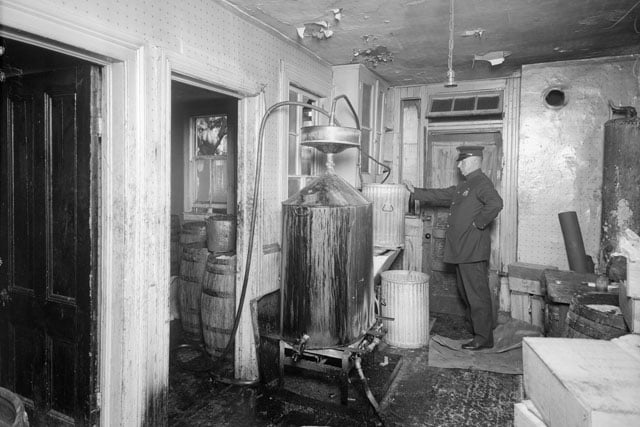 An officer examining equipment that was used to make homemade alcohol during the prohibition.