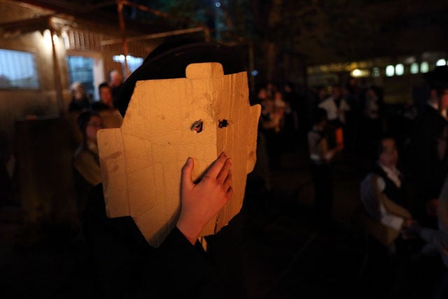 Orthodox boy watching the Lag B'Omer bonfire and using cardboard to protect himself from the heat of the fire.
