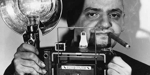 circa 1944: Polish-born American photographer Arthur Fellig (1899 - 1969) with his Speed Graphic camera. He was known by the police as 'Weegee' for his ouija-like prescience of crime scenes and disasters. In fact he kept a radio in his car tuned to the police frequency, and was often able to reach the scene before the police themselves. (Photo by Weegee(Arthur Fellig)/International Center of Photography/Getty Images)