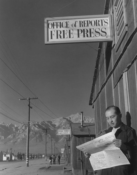 Roy Takeno reading paper in front of office.
