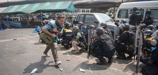 Freelance photographer KC Ortiz looks for cover during sporadic gunfire at Phan Fah bridge, Bangkok, Thailand, 18 February, 2014, during political protests. (© Nick McGrath)