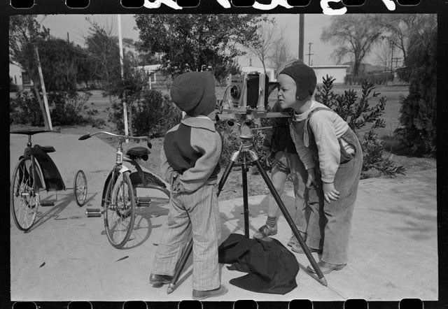 Children at the FSA (Farm Security Administration) Camelback Farms inspect the photographer's camera, Phoenix, Arizona. Photo by Russell Lee.