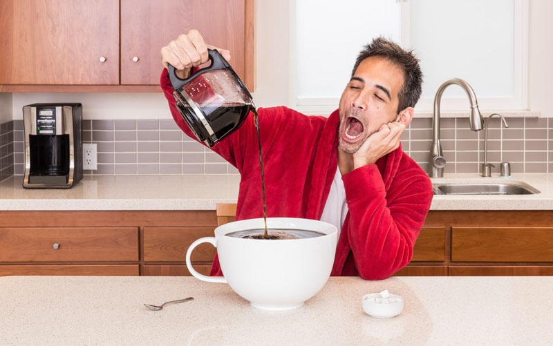 Sleepy tired man yawning in robe in kitchen pouring huge large cup of coffee