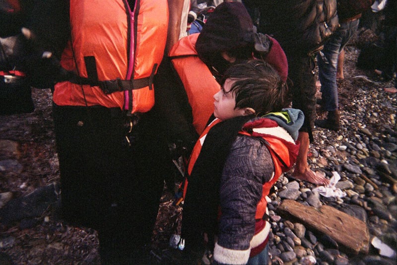 A young boy stands with his wet clothes on the stony beach right after they stranded.