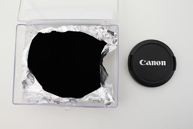 A Vantablack sheet of aluminum foil next to a Canon lens cap. Photo by Engineering & Technology