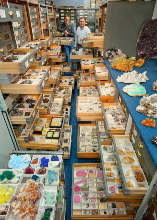 An assortment of mineral specimens from the Department of Mineral Sciences' collections are displayed in the storage vault known as the "Blue Room," at the Smithsonian Institution's National Museum of Natural History. Mineral Sciences staff present are (left) Paul Pohwat, Collections Manager of Minerals, and (right) Russell Feather, Collections Manager of Gems.