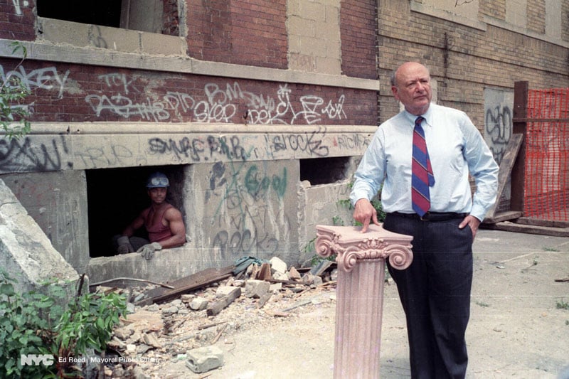 A construction worker looks on as Mayor Koch makes an announcement regarding housing in 1989.