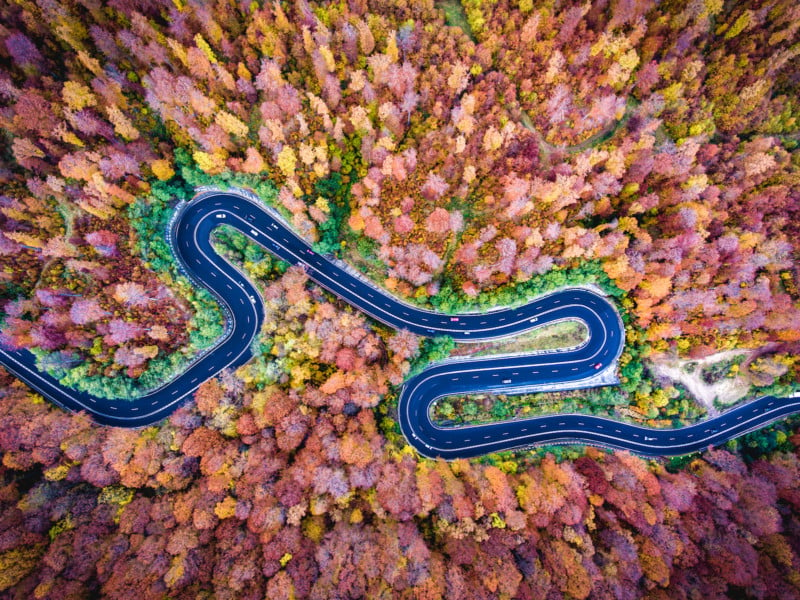 Aerial drone view of a curved winding road through the forest high up in the mountains
