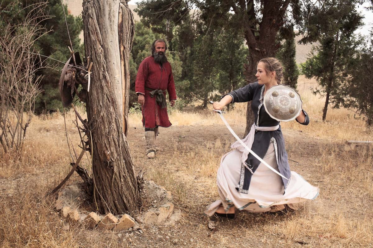 Anna practicing sword fighting on a dead tree as Ali watches her movements and makes sure she hits the tree properly. The swords are heavy and it's easy to get hurt practicing sword fighting. They're both wearing traditionnal clothing.