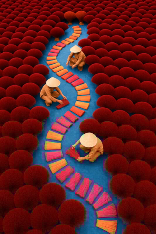 Three people in conical hats arrange bundles of colorful incense sticks in a winding line on a blue surface, surrounded by densely packed red incense bundles.