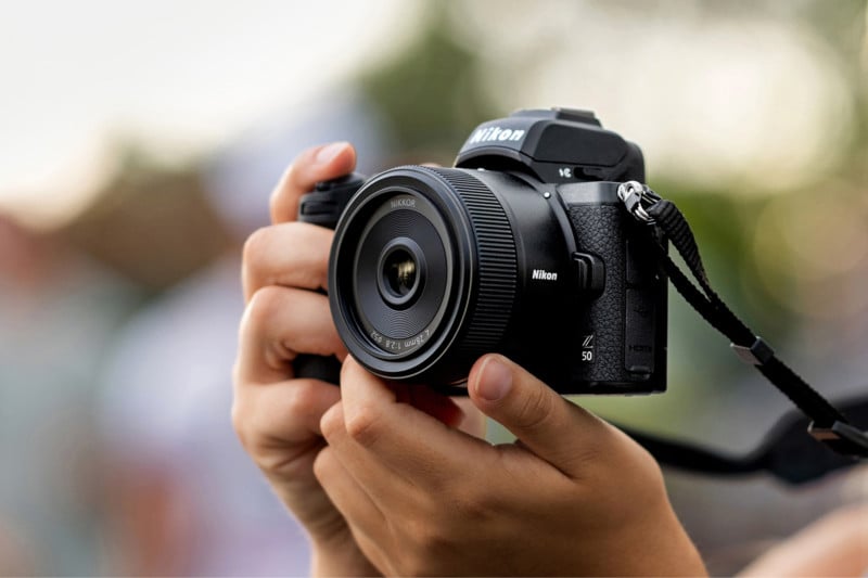 The Nikon 28mm f/2.8 lens attached to a camera and held by two hands